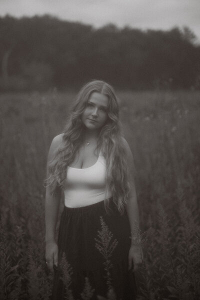 Black and white, moody and vintage looking senior photography captured by Morgan Ashley Lynn Photography in Lake Country, WI of a girl standing in a field of wildflowers looking at the camera and not smiling