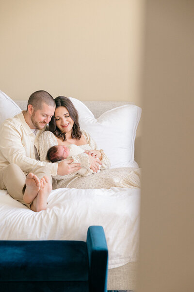 mother and father dressed in creams look down lovingly at their newborn baby girl, in home Indianapolis photography