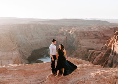 man and woman standing on cliff with canyon in the background