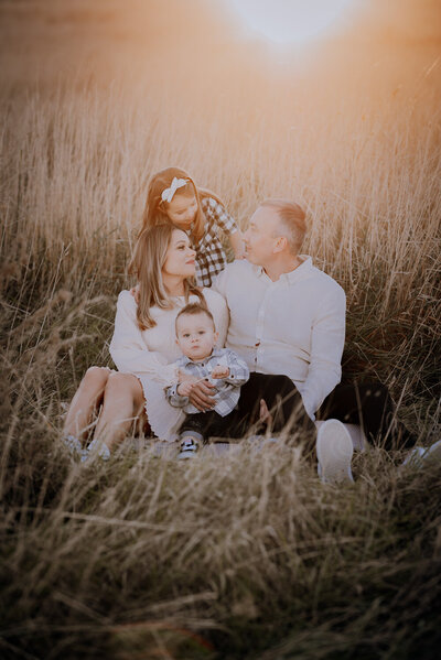 Family of four sitting in a field of long grass with sun flare from the top of the image