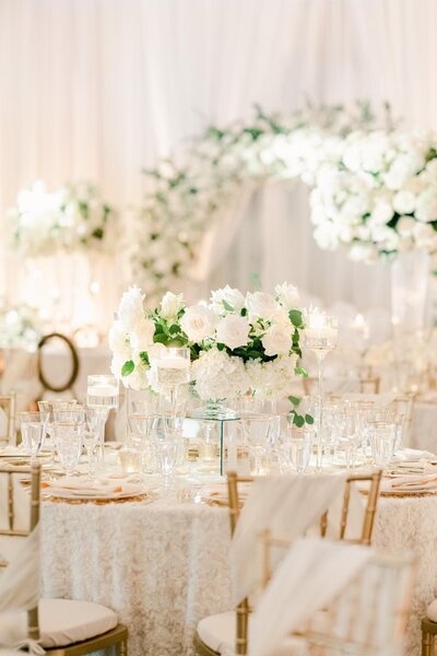 An elegant wedding reception setup with white floral centerpieces, transparent glassware, and chiavari chairs, captured by a luxury wedding photographer.