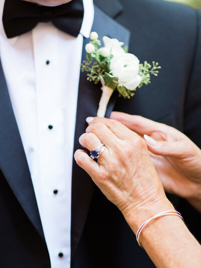 Mother of groom pinning groom's boutonniere with white flowers and greenery