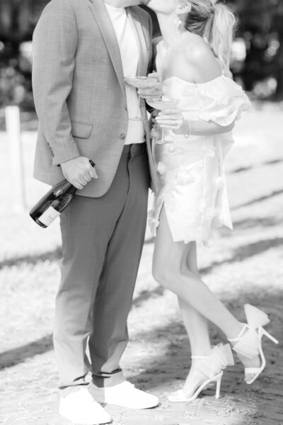 Black and white photo of a couple holding glasses of champagne and kissing during their St. Augustine engagement session