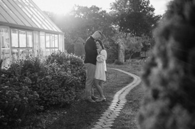 In a romantic scene, a couple stands by a quaint house with a winding path, and the guy affectionately kisses the girl on the crown
