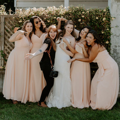 photographer standing with bride and bridesmaids while laughing