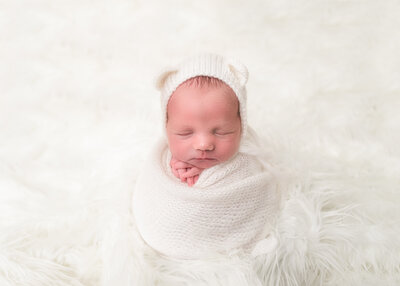 newborn wrapped in white wrap and bear bonnet in kelowna studio