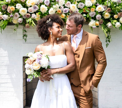 Bride and Groom in front of a white outdoor fireplace adorned with spring pastel florals on the mantel.