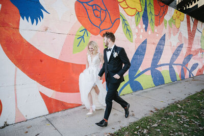 bride and groom running in front of colorful mural in downtown Grand Rapids Michigan