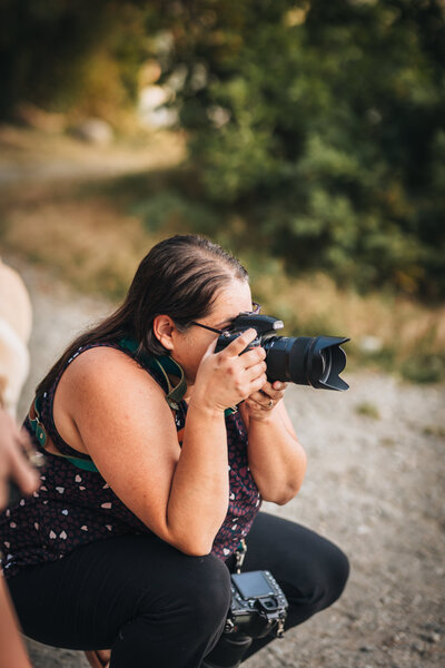 Photographer bending down looking through her Nikon camera.