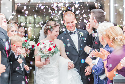 Bride and groom smile bright while leaving their wedding ceremony while being showered in bubbles by their guests