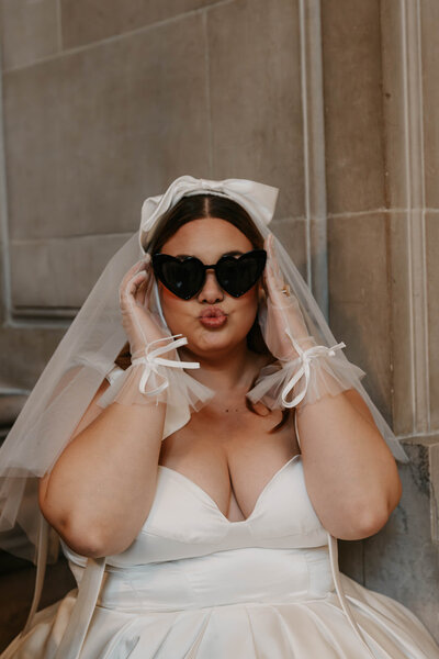 Bride in a white dress and veil poses playfully, wearing heart-shaped black sunglasses and making a kissy face—capturing the fun, candid spirit found in playful family photos in Montrose Colorado.