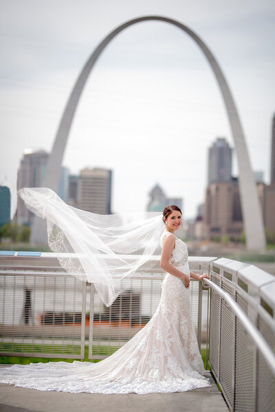 Beautiful bride in her wedding dress with veil trailing in the wind under the arch in St Louis