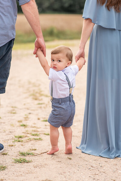 Baby boy holding parents hands, looking back at the camera