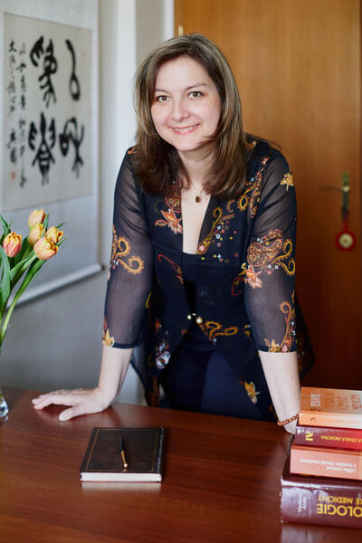 Zuzana standing by her desk with Chinese scroll behind her  in her office in Prague