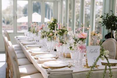 Refined orangery wedding table setting with elegant gold-rimmed plates and delicate pink floral centerpieces.