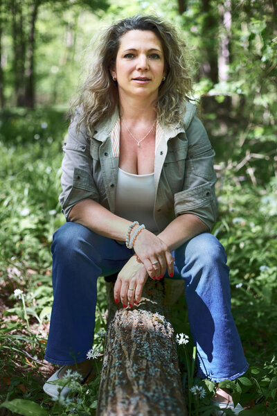 Sarka, a life coach from Brno, sitting on a log in the forest, looking to camera