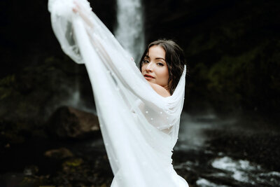 beautiful bride is playing with her vail in front of a waterfall in Iceland