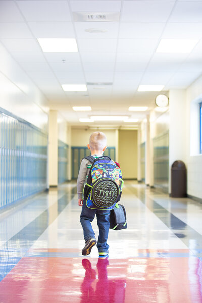 boy with backpack and lunch box walking the halls of school