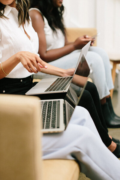 Three women sitting on a sofa working with their laptops and a cellphone.