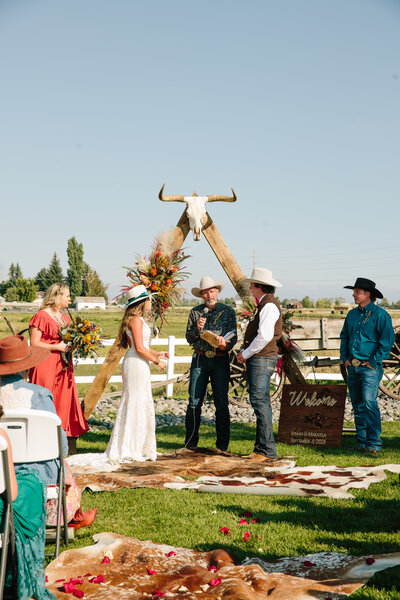 bride and groom standing together wearing  cowboy hats during western inspired ceremony