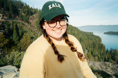 Ashley, a Minnesota wedding photographer, wearing a yellow sweatshirt, green cap that says kale, in Lake Tahoe on 35mm film.