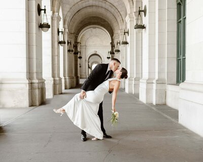 Groom dips bride and kisses her while standing under the arches of Union Station during their Washington DC elopement.