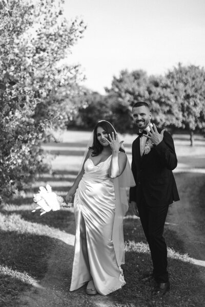 Black and white photo of a bride and groom waving, with a nature backdrop.