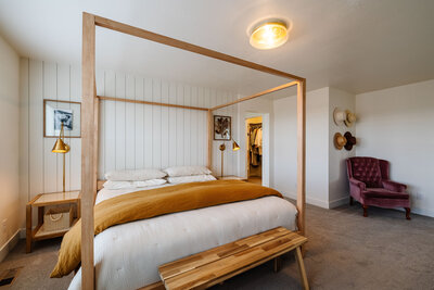 Primary bedroom in a Northern Colorado home, featuring a modern wood canopy bed, neutral bedding, and minimalist decor—staged by Haug & Co. for real estate listing.