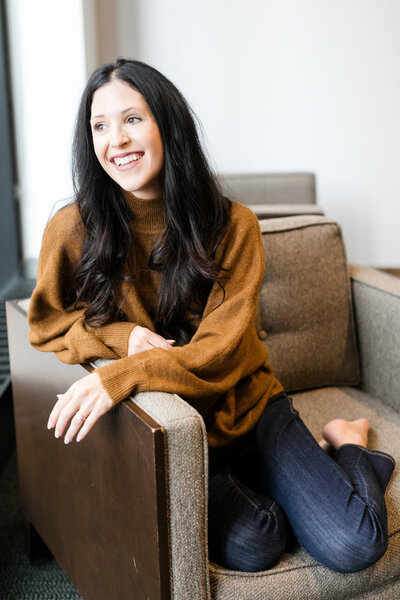 Woman sitting with legs folded on a chair, smiling.