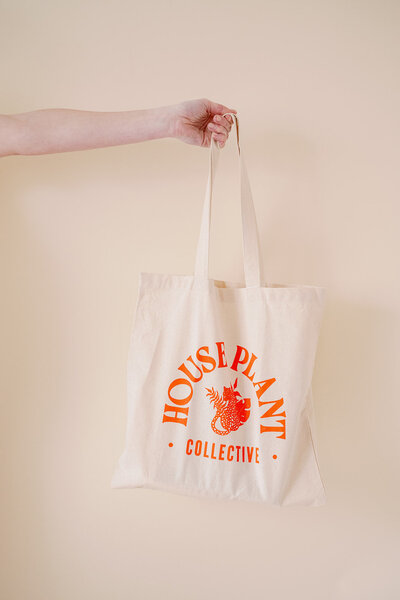 Arm holding a canvas tote bag with the House Plant Collective logo on it