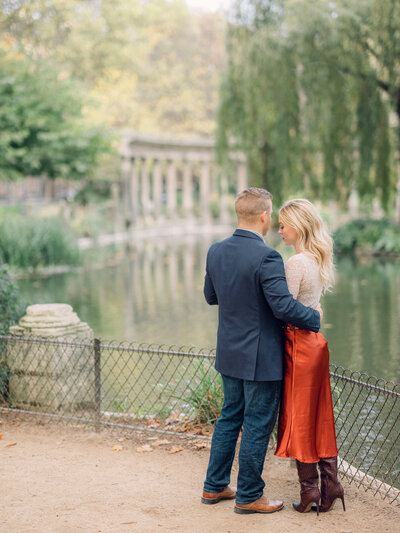 a blonde couple with their backs towards to camera looking off into the distance at parc monceau in paris
