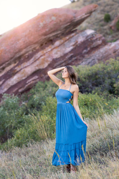 Senior girl in a blue dress standing on a field with rock montain behind