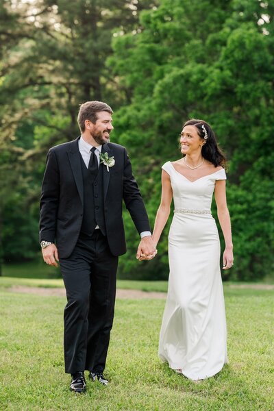 groom and bride holding hands on wedding day walking in grass