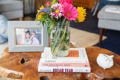Flowers in a mason jar sitting ontop of a stack of books with a fram on the left.