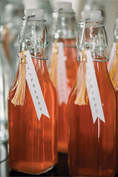 Colorful pink-themed individual drinks with personalized tag labels and custom tassels, beautifully arranged for a girl’s baby shower.
