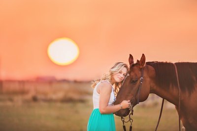 Beautiful high school senior girl  with her horse  at sunset