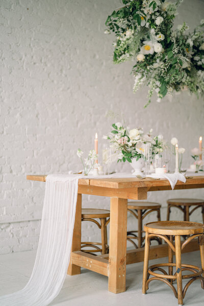 a wooden table with a white draped table cloth down the middle and white florals and candles on the table