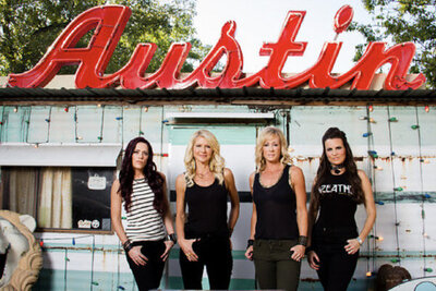 Band portrait female music group The Mrs standing against building with the sign Austin written in red above them