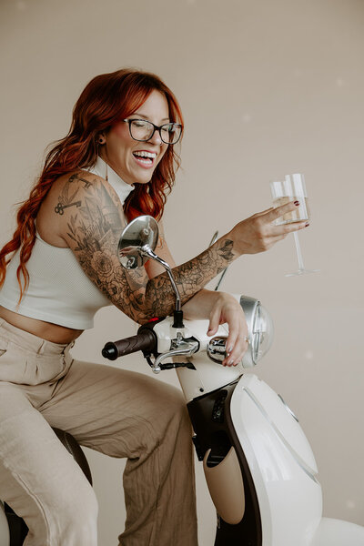 woman with red hair sitting on a white scooter holding champagne