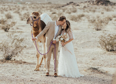 couple embracing next to camel in joshua tree