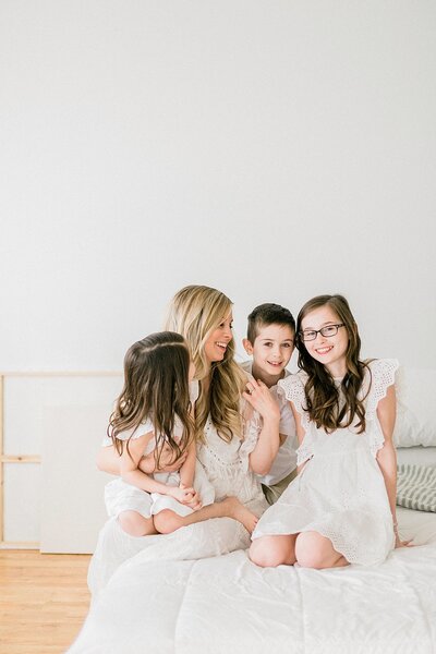 Jess Becker Photography sitting on a bed with her three children as everyone smiles