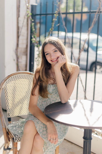 Sixteen birthday girl sits at coffee shop table on patio in Galveston while wearing a green dress at sunrise