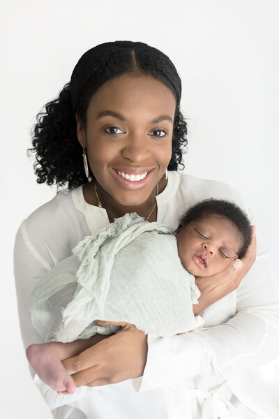 African American mom smiling while snuggling her newborn baby boy swaddled in soft green fabric
