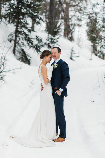 A bride and groom snuggle together on a snowy trail outside of Grand Teton National Park on their elopement day photographed by Amy Galbraith