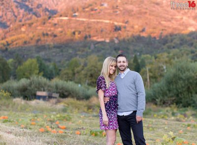 Engaged couple cozy up to each other as they pose for the engagement photographer in Riley's Los Rios Rancho in Oak Glen