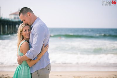 Engaged couple fully embrace one another during engagement photo session next to the Manhattan Beach Pier