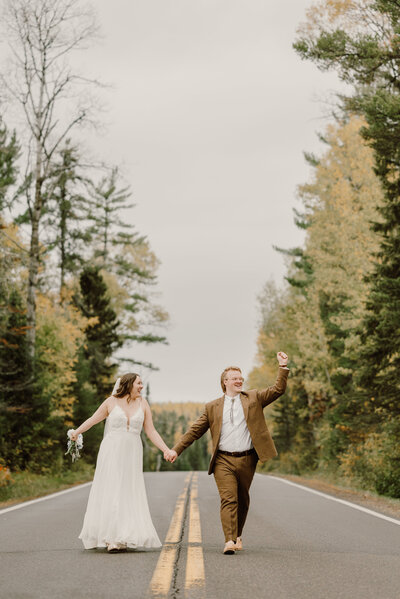 Bride and groom running down the road through a tunnel of pine trees