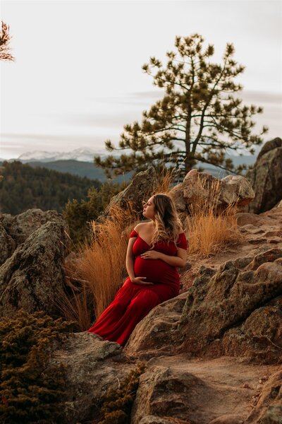 Pregnant woman in red dress sitting on rocks on top of Lost Gulch Overlook