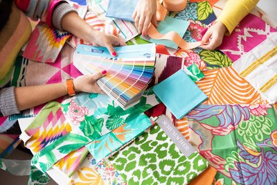 Two sets of hands look through colorful swatches and fabrics.
