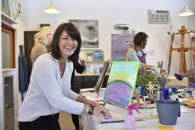 woman smiling while standing at a table painting